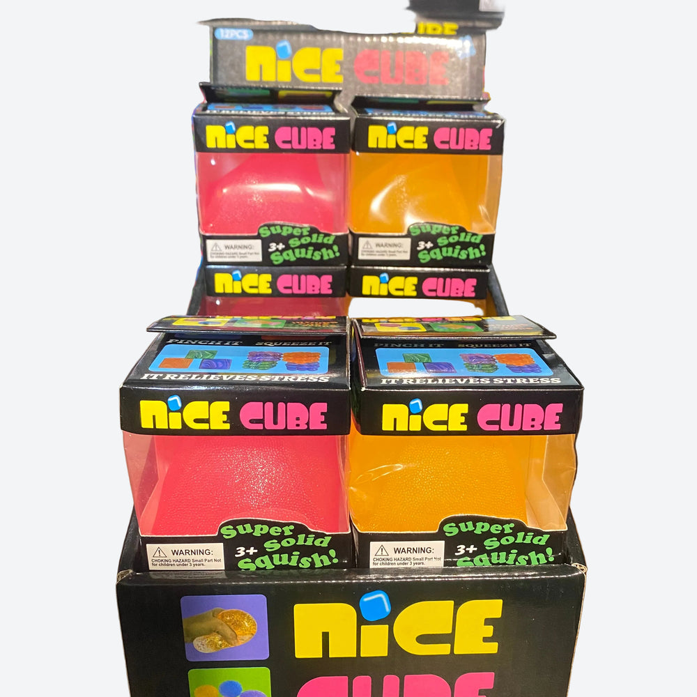 A retail display of NICE CUBE stress-relief squishy toys in black packaging, featuring translucent pink, red, and orange cubes on a wooden shelf.
