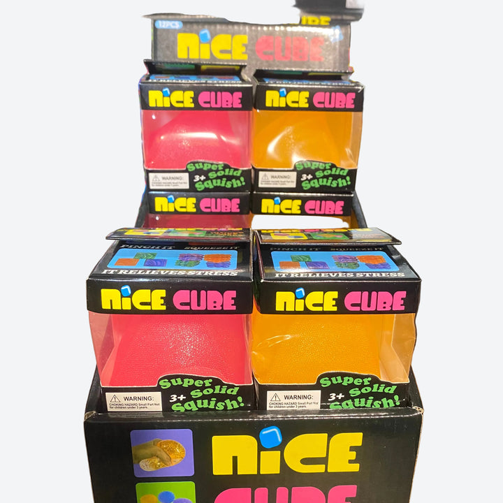 A retail display of NICE CUBE stress-relief squishy toys in black packaging, featuring translucent pink, red, and orange cubes on a wooden shelf.