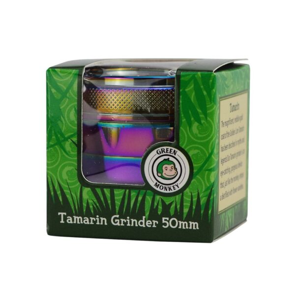 A 50mm tamarin grinder in its original green packaging box, featuring a clear window that displays the metallic iridescent grinder inside. The packaging has green leaf patterns, a circular 'Green Monkey' brand logo, and text identifying it as a 'Tamarin Grinder 50mm'.