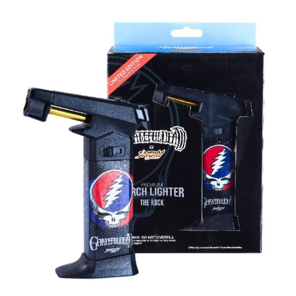 A black Grateful Dead 'The Rock' torch lighter shown in front of its retail packaging box. The lighter features the iconic red, white, and blue Grateful Dead skull logo on the side.