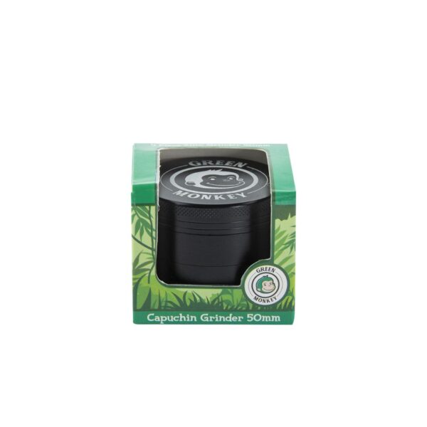 A black capuchin grinder in its green retail packaging, featuring a clear window that displays the grinder. The packaging has green leaf patterns and a circular sticker that reads 'Guilty Monkey'.
