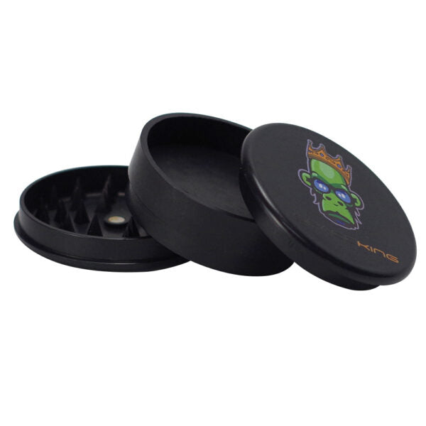 A black metal herb grinder with a three-piece lid design, shown open on a plain white background. The top lid features a colorful graphic of a green monkey wearing a gold crown and the brand name 'Kings' in gold.
