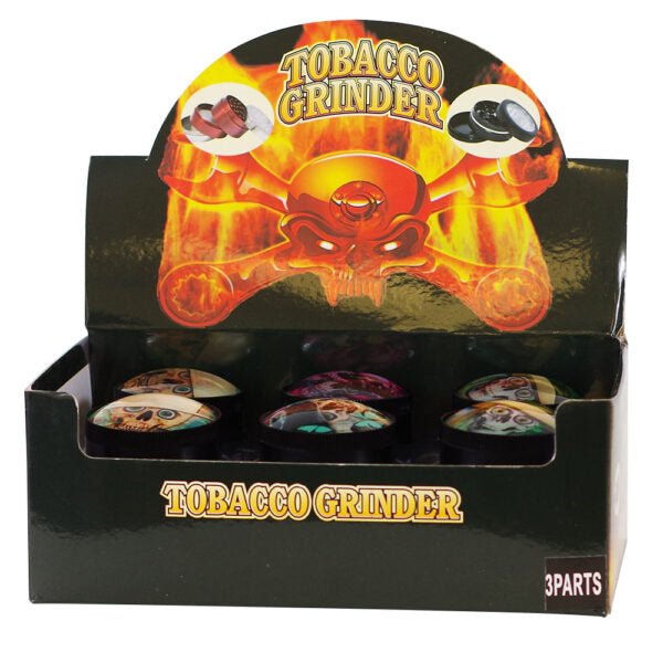 A black retail display box labeled 'TOBACCO GRINDER' with a large fiery orange skull graphic on the front. Several small round tobacco grinder cans are visible inside the open display, and a small '3PARTS' label appears in the bottom right corner.