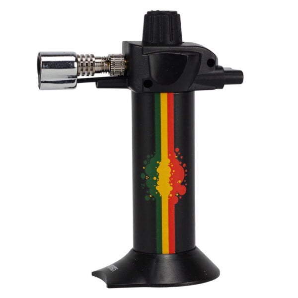 A black torch lighter with a Rastafarian flag-inspired vertical stripe pattern in green, yellow, and red on the main body, featuring a silver metal nozzle on the left and a black adjustment knob on top, set against a plain white background.