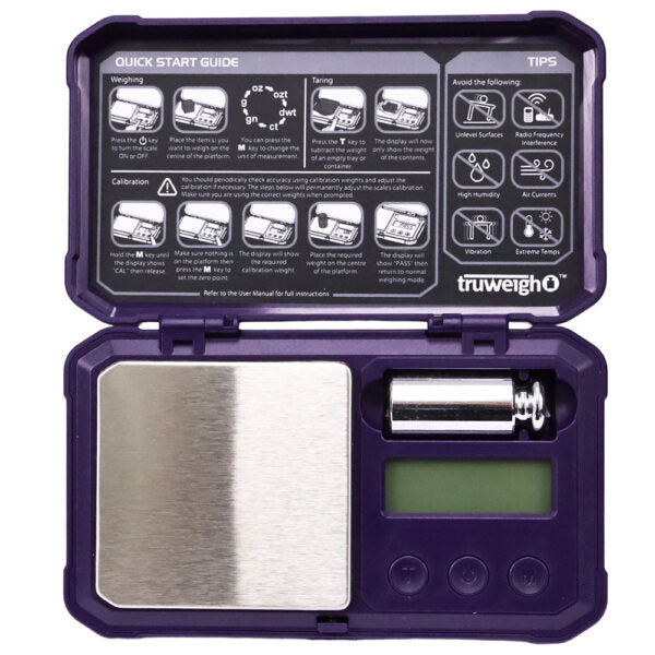 A compact digital pocket scale in a dark purple case, shown open with the lid displaying a quick start guide and tips. The scale features a brushed stainless steel weighing platform, a small green LCD screen, and a metal weight inside a slot on the right.