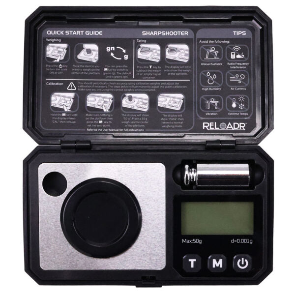 A portable digital pocket scale shown open, with the lid displaying an illustrated quick start guide and the base showing a silver and black weighing platform, a digital LCD screen, and accessories including a metal weight and a spring. The brand name 'RELOAD' is visible on the inside of the lid.