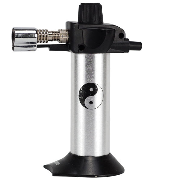 A portable torch lighter with a brushed silver aluminum body, black plastic top and base, and a black-and-white yin-yang symbol printed on the front. It features a silver metal nozzle on the left and a black adjustment knob on top, all set against a plain white background.