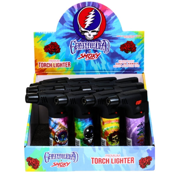 A retail display box filled with black Grateful Dead Smoky torch lighters, with a colorful tie-dye branded header card and front panel on a white background.