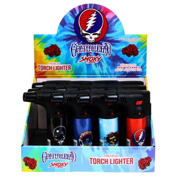 A retail display box of Grateful Dead Smoky branded torch lighters. The box features a colorful tie-dye background with the Grateful Dead skull logo and red roses, holding four black torch lighters with blue, light blue, and red bodies decorated with Grateful Dead graphics.