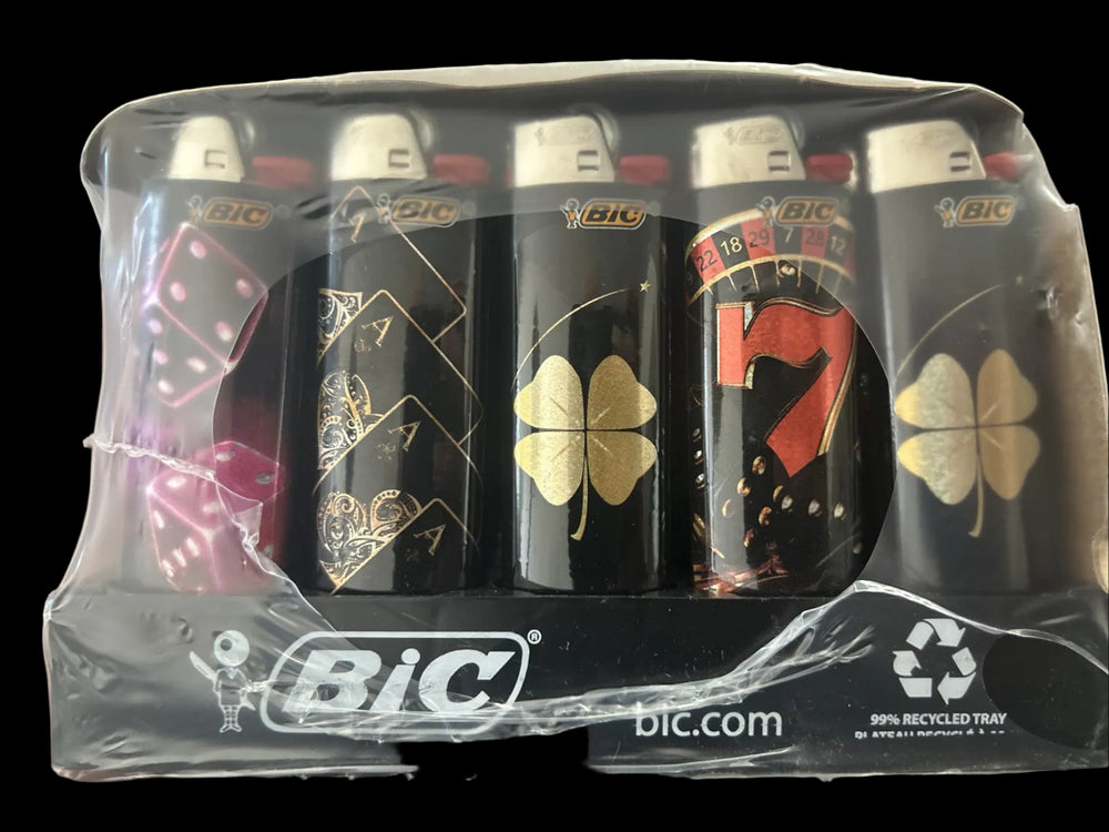 A set of five BiC novelty lighters in a clear plastic clamshell package. The lighters feature black backgrounds with various designs including a pink dice face, playing card suits, a gold four-leaf clover, a red and black roulette wheel, and a gold four-leaf clover.
