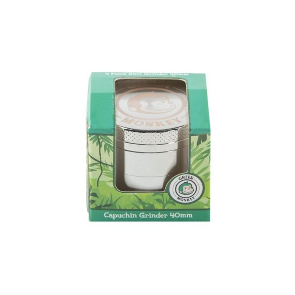 A silver metal capuchin grinder in its green retail packaging, featuring a window that displays the cylindrical grinder and a circular 'Oliva Monkey' logo.