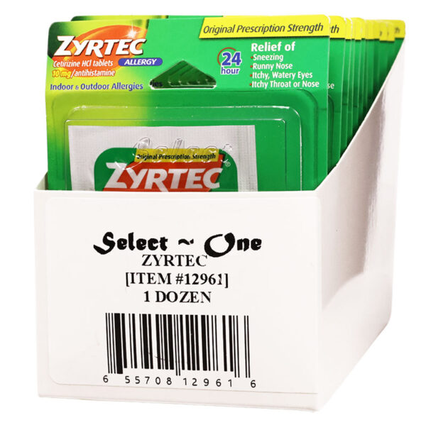 A white cardboard retail display box holding multiple Zyrtec allergy relief packets. The packets are green with orange and white branding, and the front of the box reads 'Select One Zyrtec [ITEM #12961] 1 DOZEN' with a barcode.