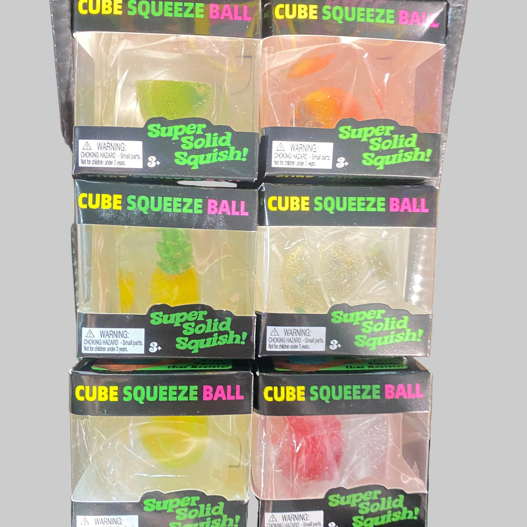 Six packages of Super Solid Squishy Cube Squeeze Ball toys arranged in a 2x3 grid on a wooden surface. The packages contain translucent gummy-like balls shaped like citrus fruits, including lime, orange, pineapple, and lemon, visible through clear plastic windows with black labels reading 'Super Solid Squishy!'.