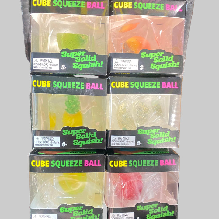 Six packages of Super Solid Squishy Cube Squeeze Ball toys arranged in a 2x3 grid on a wooden surface. The packages contain translucent gummy-like balls shaped like citrus fruits, including lime, orange, pineapple, and lemon, visible through clear plastic windows with black labels reading 'Super Solid Squishy!'.