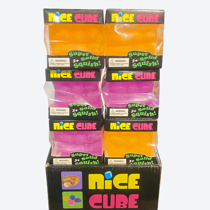 A retail display box filled with multiple packaged 'Nice Cube' squishy toys in assorted colors, including orange, pink, and yellow, on a wooden store shelf.