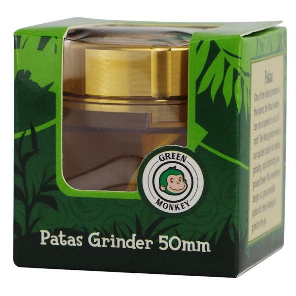 Green Monkey Patas Grinder 50mm shown inside its green branded cardboard packaging box, featuring a gold-colored metal grinder visible through a clear plastic window.