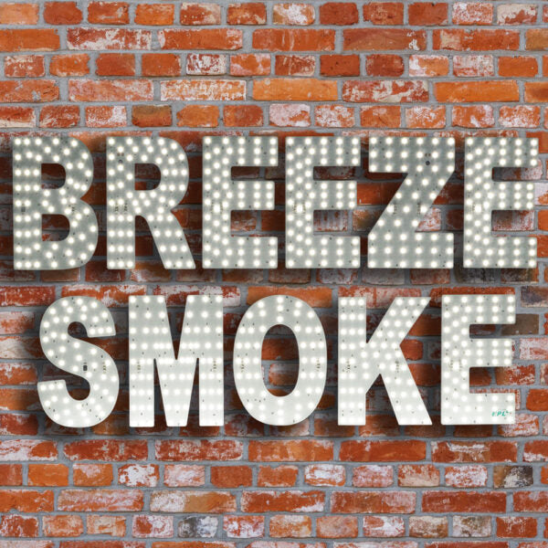 Lighted marquee-style letters spelling “BREEZE SMOKE” mounted against a red-orange brick wall background.