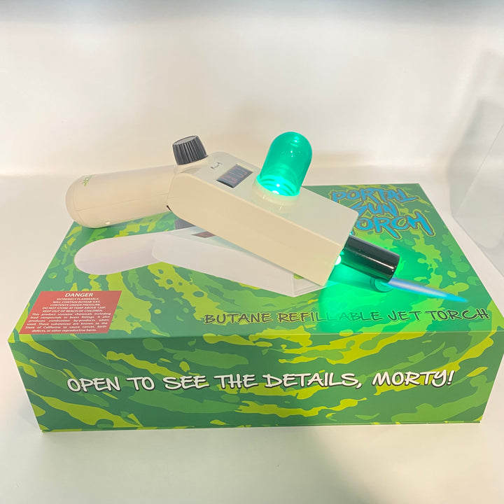 Off-white Portal Gun jet torch with glowing green LED dome, resting on a green sci-fi themed product box.