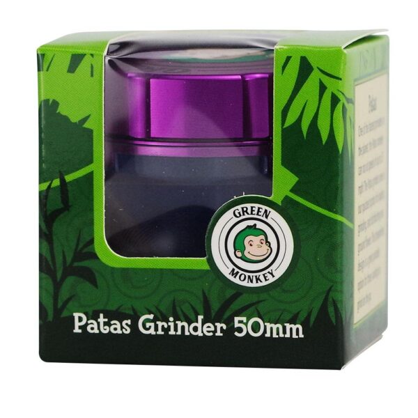 Patas Grinder 50mm in its original green and black packaging with a clear window showing the purple grinder inside. The packaging features the Green Monkey brand logo and a jungle leaf pattern.