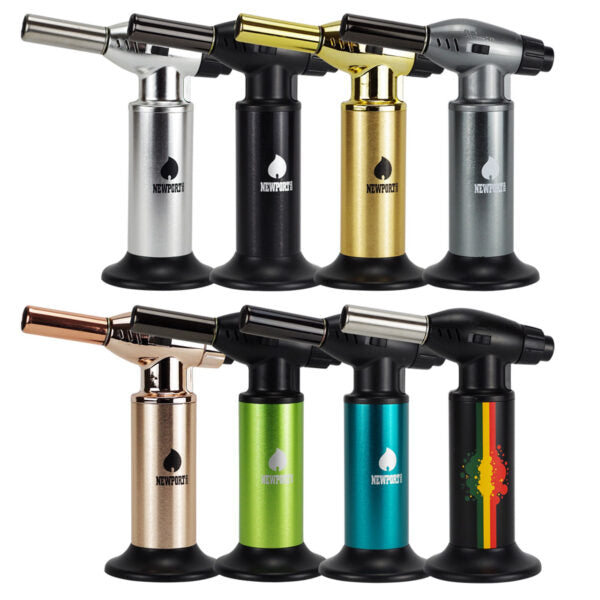 Six torch lighters arranged in two rows of three on a plain white background. The lighters have black bases and bodies with metallic finishes in silver, gold, rose gold, green, blue, and a black body with a red, yellow, and green graphic.