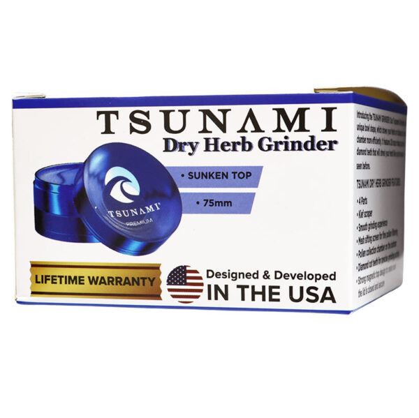 Tsunami Dry Herb Grinder in its retail packaging, featuring a white box with blue and black text, a graphic of the blue metal grinder, and a 'Designed & Developed in the USA' banner.
