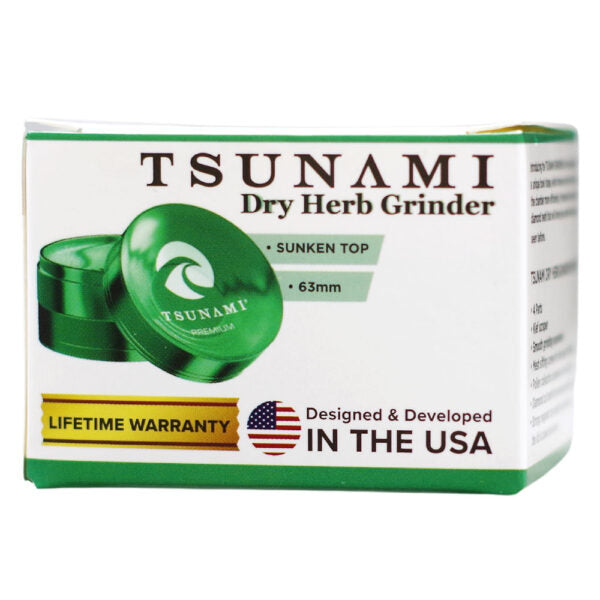 Tsunami Dry Herb Grinder packaging box in white and green, featuring a graphic of the green metal grinder lid and text including 'TSUNAMI Dry Herb Grinder', 'Sunken Top', '63mm', and 'Lifetime Warranty'.