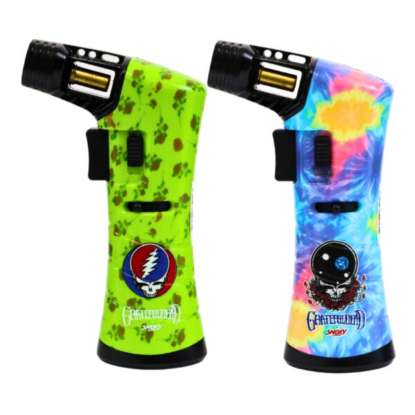 Two Grateful Dead torch lighters shown side by side on a white background. The left lighter has a bright lime green body with brown splatter patterns and the Grateful Dead skull logo.