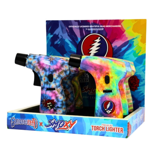 Two Grateful Dead x Smokey 'Fire Up Torch Lighter' torch lighters displayed in their retail box. The lighters feature a vibrant tie-dye pattern in blue, pink, yellow, and green, with black tips and Grateful Dead skull-and-ribbon logos.