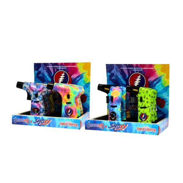 Two retail display boxes containing multiple Grateful Dead x Smoxy torch lighters with colorful tie-dye and patterned designs, set against a plain white background.