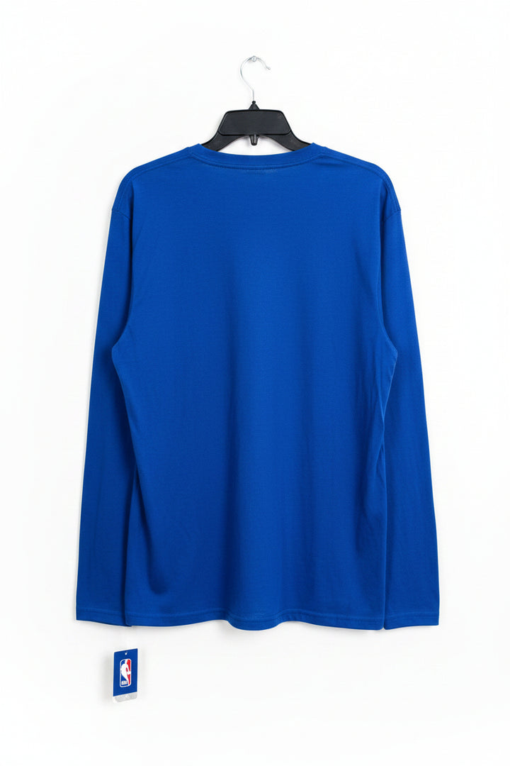 A royal blue long-sleeve t-shirt hanging on a black hanger against a wooden door, with other garments partially visible on the left.